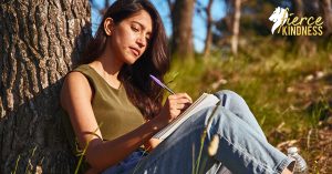 Woman with journal leaning against tree for journaling quotes