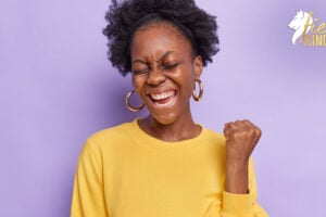 Woman with raised fist saying Yes in yellow top against lilac background