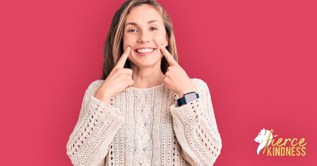 Woman forcing a smile with fingers to show being nice and am I a people pleaser on deep pink background