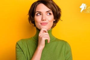 Woman in green sweater pondering, holding chin looking up and right