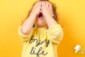 Child covering face looking horrified and guilty wearing yellow shirt