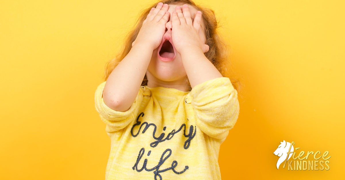 Child covering face looking horrified and guilty wearing yellow shirt